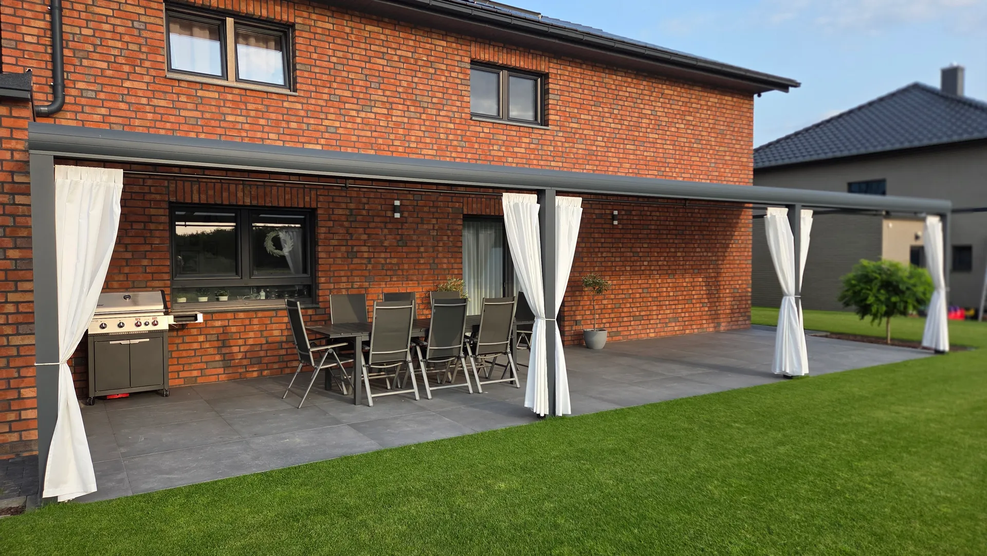 Terrassenüberdachung an einem Klinkerhaus, helle Vorhänge zwischen den Pfosten, Wolfsburg